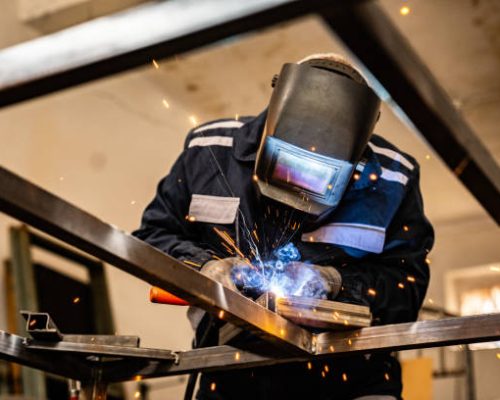 senior man welding at his work place. he is dressed in work suit.