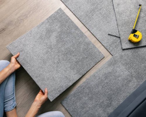 woman laying carpet tiles on floor in living room. diy home improvement